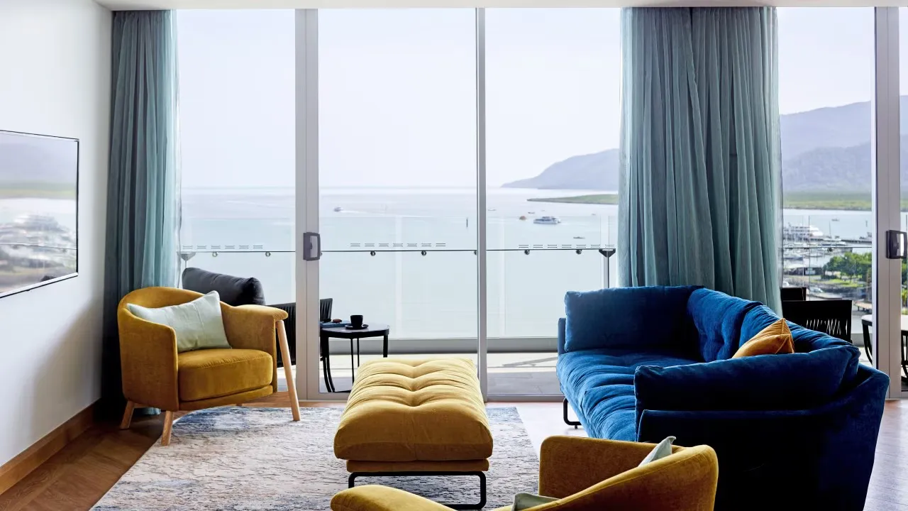 Apartment lounge with mustard and blue velvet seating opening onto a harbour view