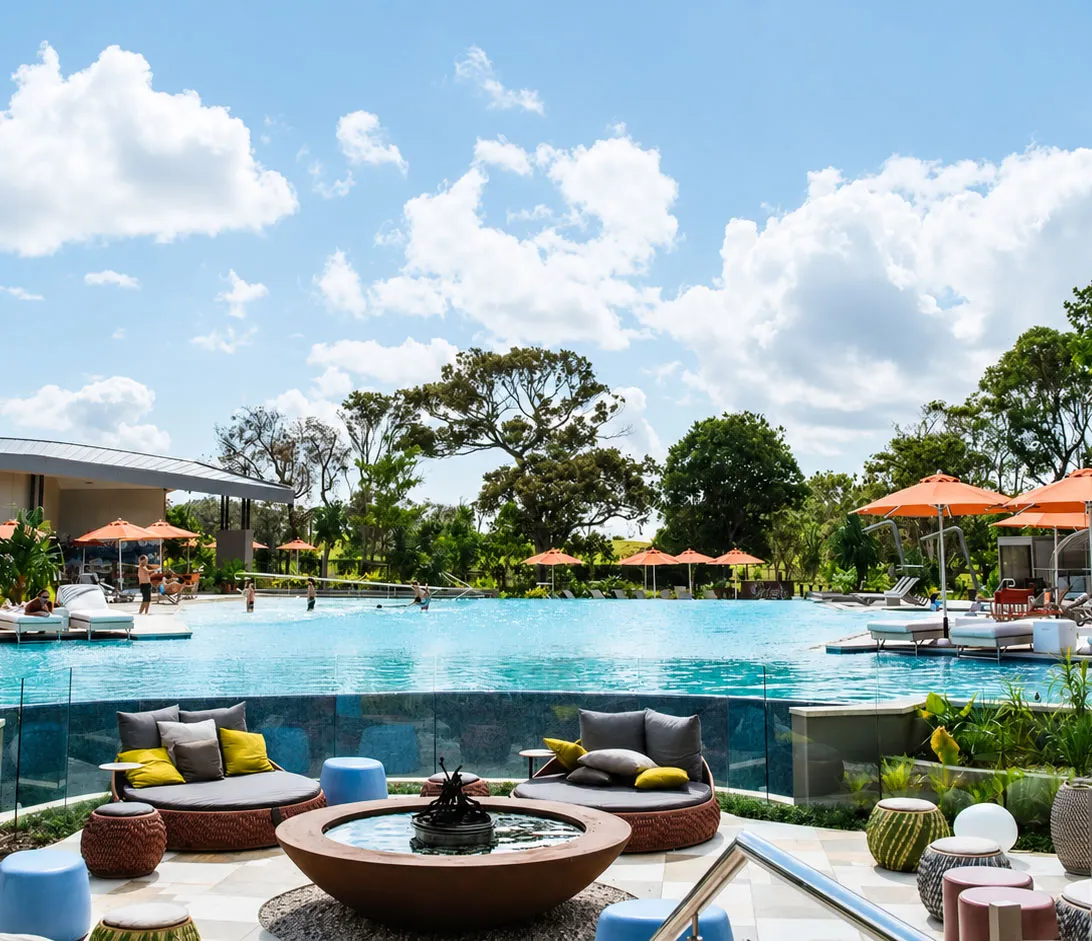 Resort pool at Elements of Byron ringed by sun lounges, orange umbrellas and daybeds under a blue sky