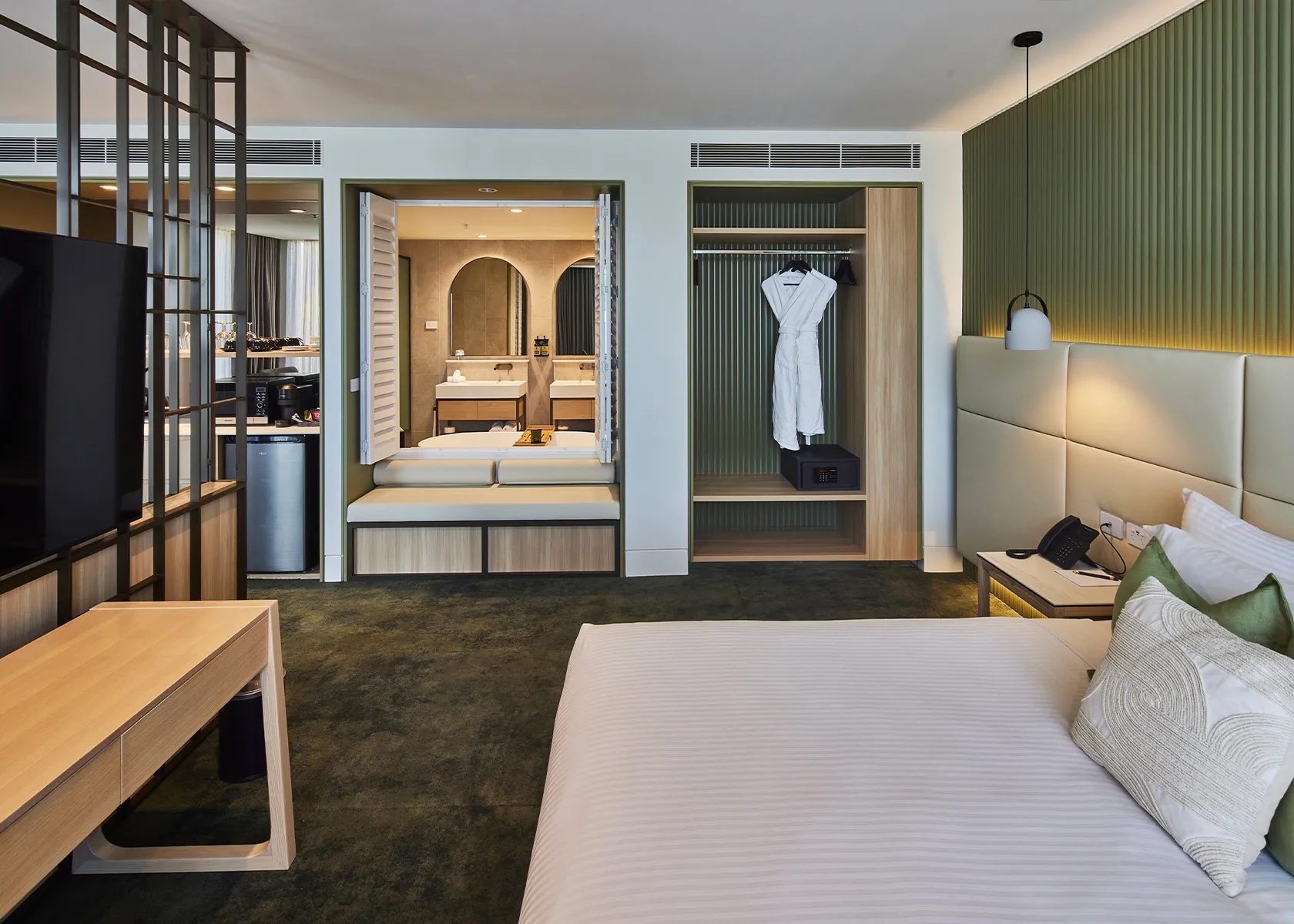 Hotel bedroom with a fluted olive-green feature wall, an open robe cupboard and the bathroom beyond
