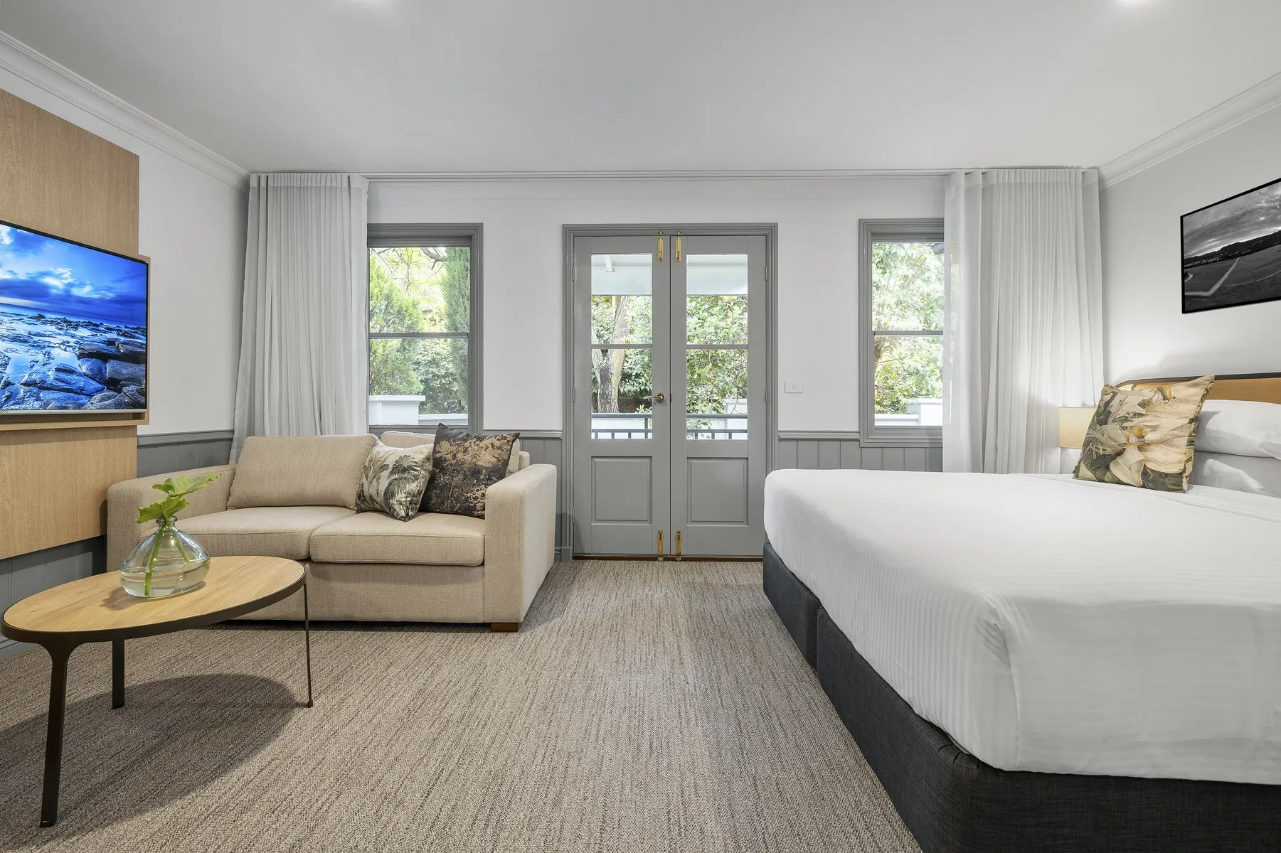 Hotel suite with a sofa and bed beside French doors onto a garden