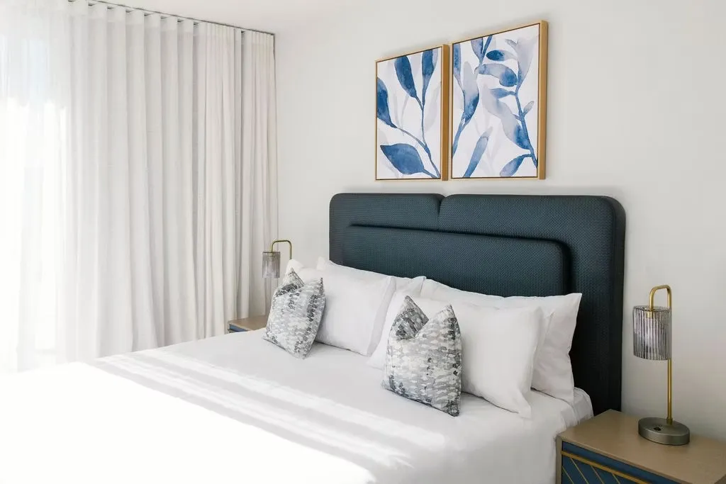 Hotel bed with a navy upholstered bedhead and framed botanical prints