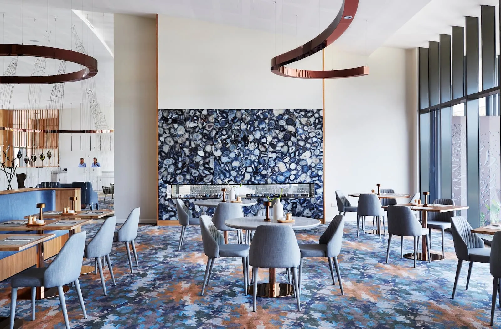 Hotel restaurant with blue upholstered dining chairs, patterned carpet and a backlit blue agate feature wall
